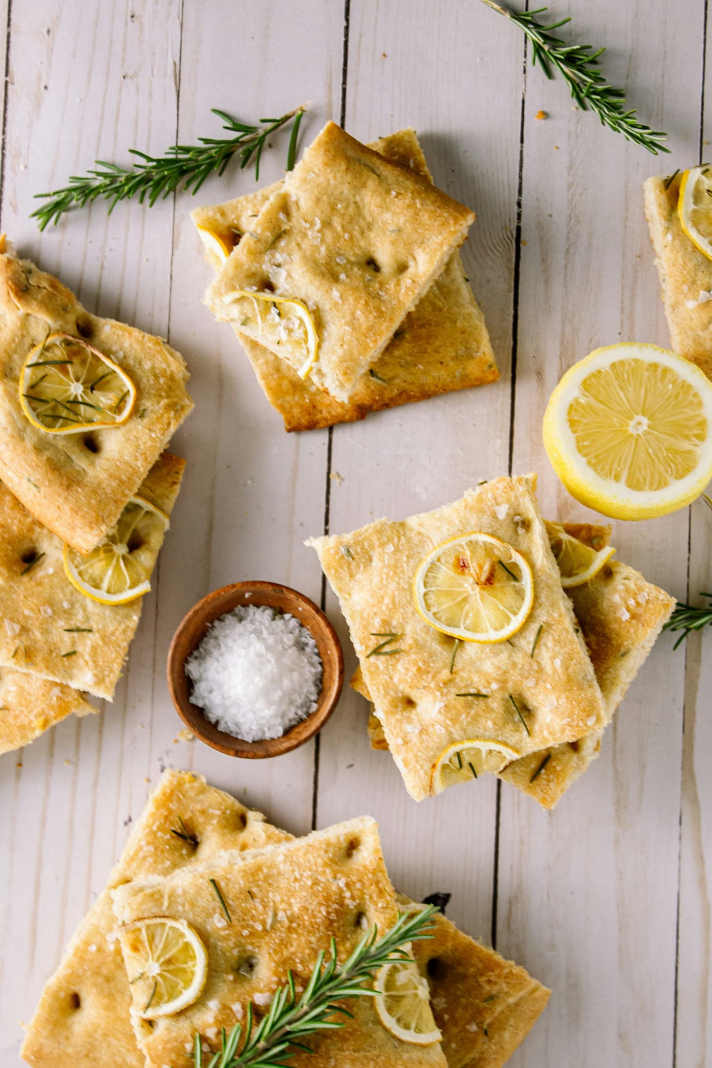 Squares of rosemary focaccia on a pale wooden board with flaked salt