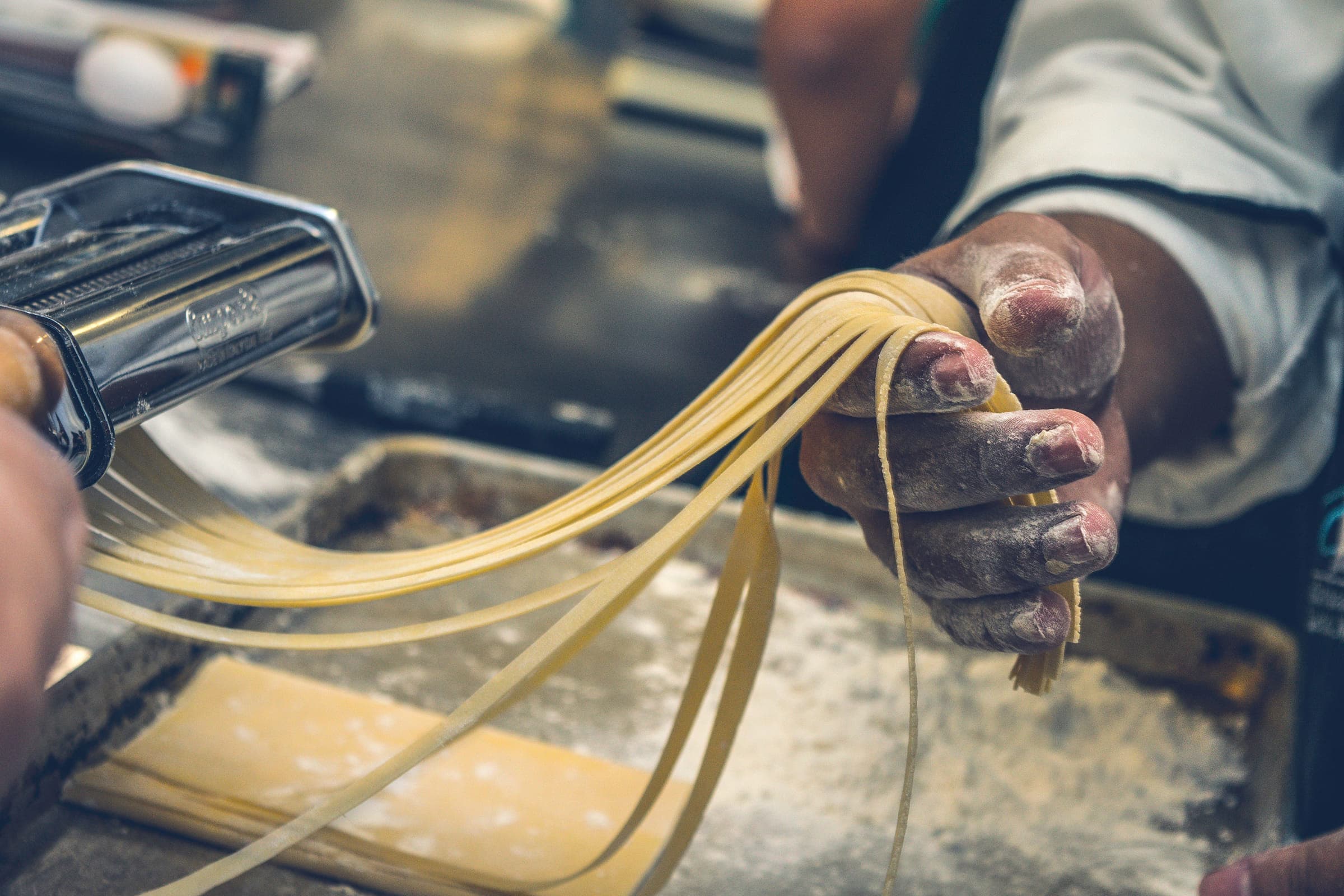 A cook lifting a ribbon of fresh tagliatelle from the pasta machine
