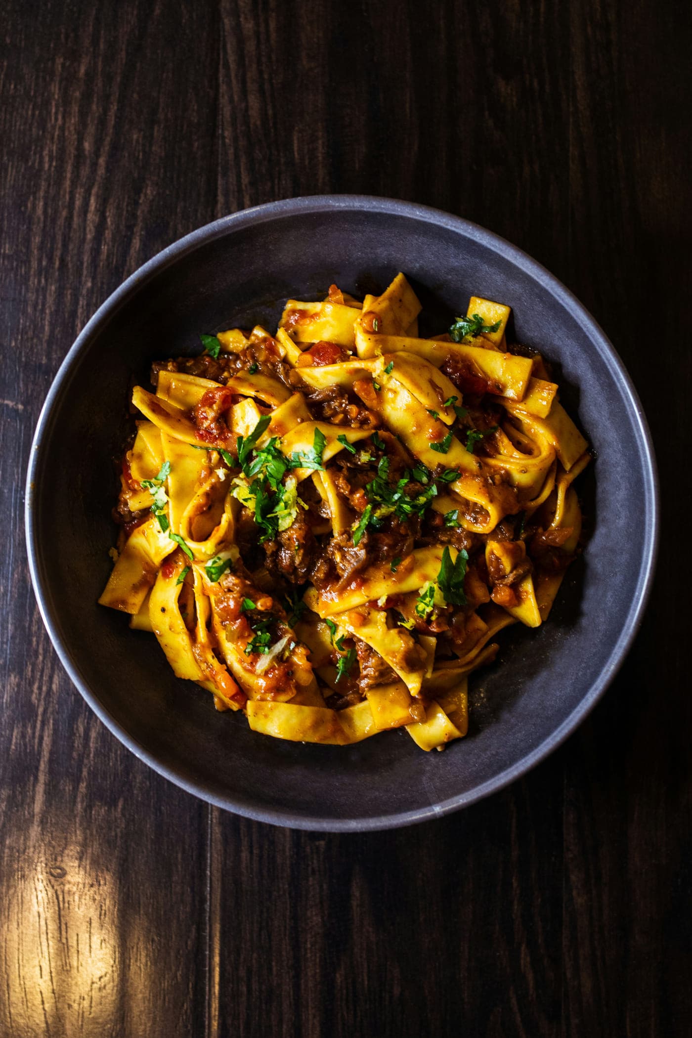 Wide pappardelle ribbons under a dark meat ragu, scattered with parsley