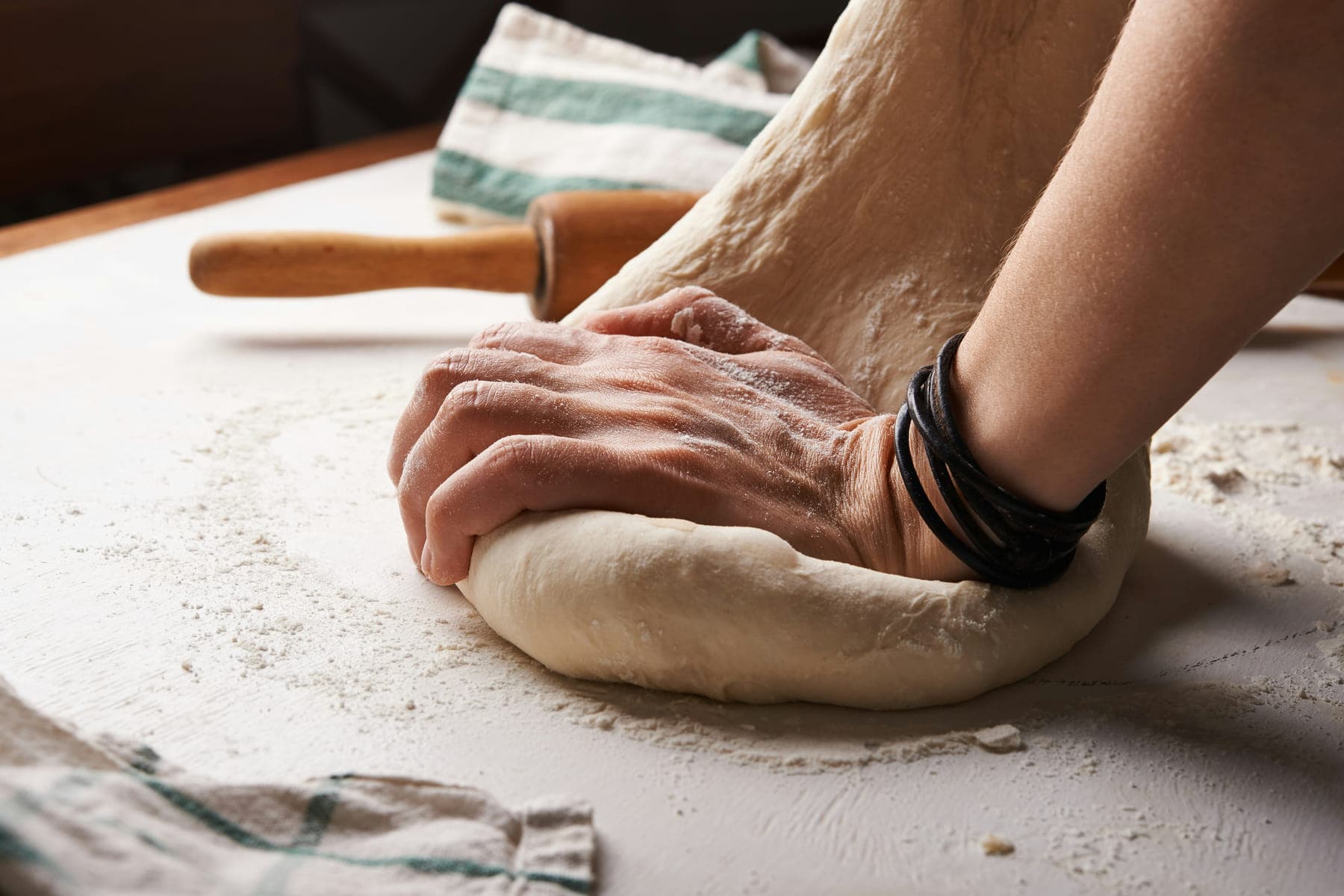 Hands working a mound of pasta dough on a floured bench