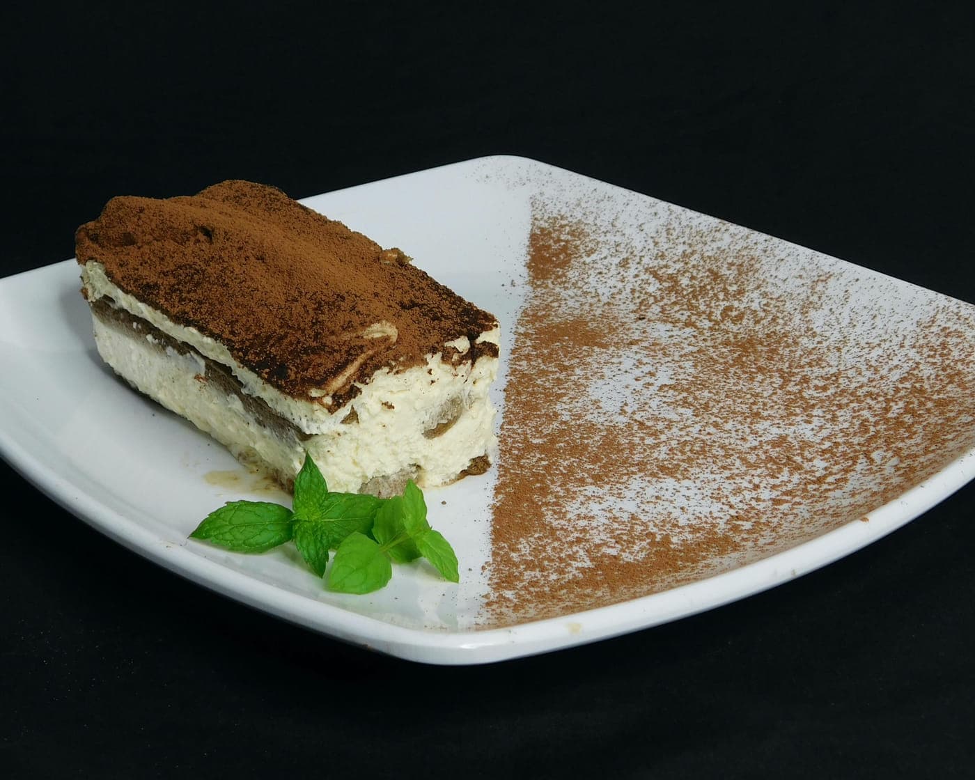 A slice of tiramisu dusted with cocoa on a white plate