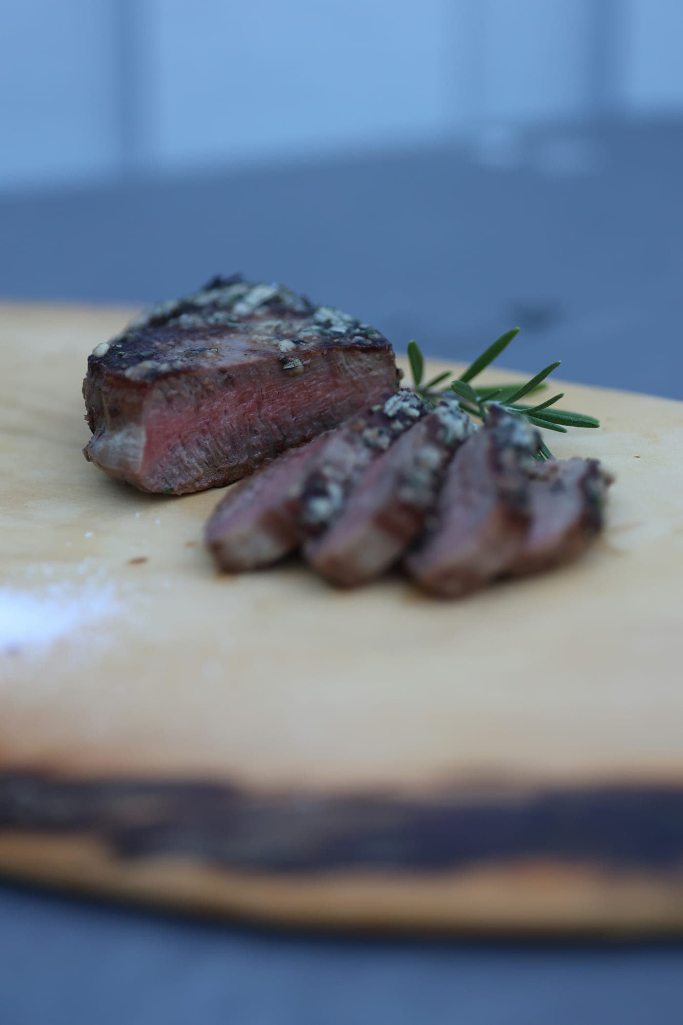 A sliced, rested sirloin with rosemary on a carving board