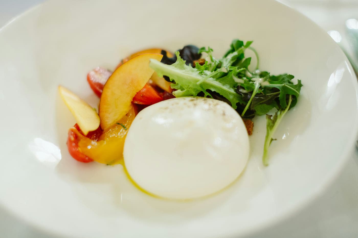 A ball of burrata with tomato and rocket on a white plate