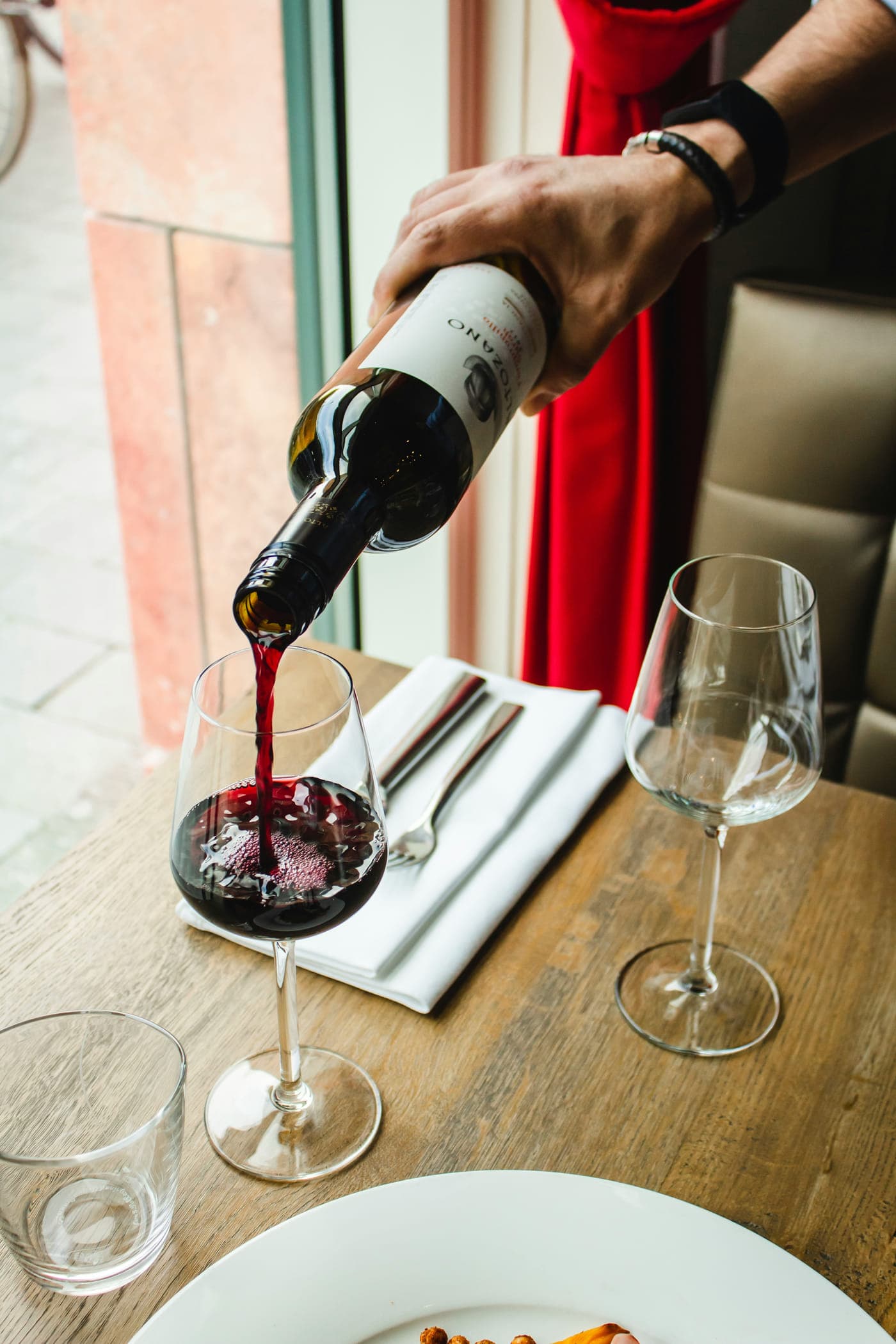 Red wine being poured into a glass at a laid table