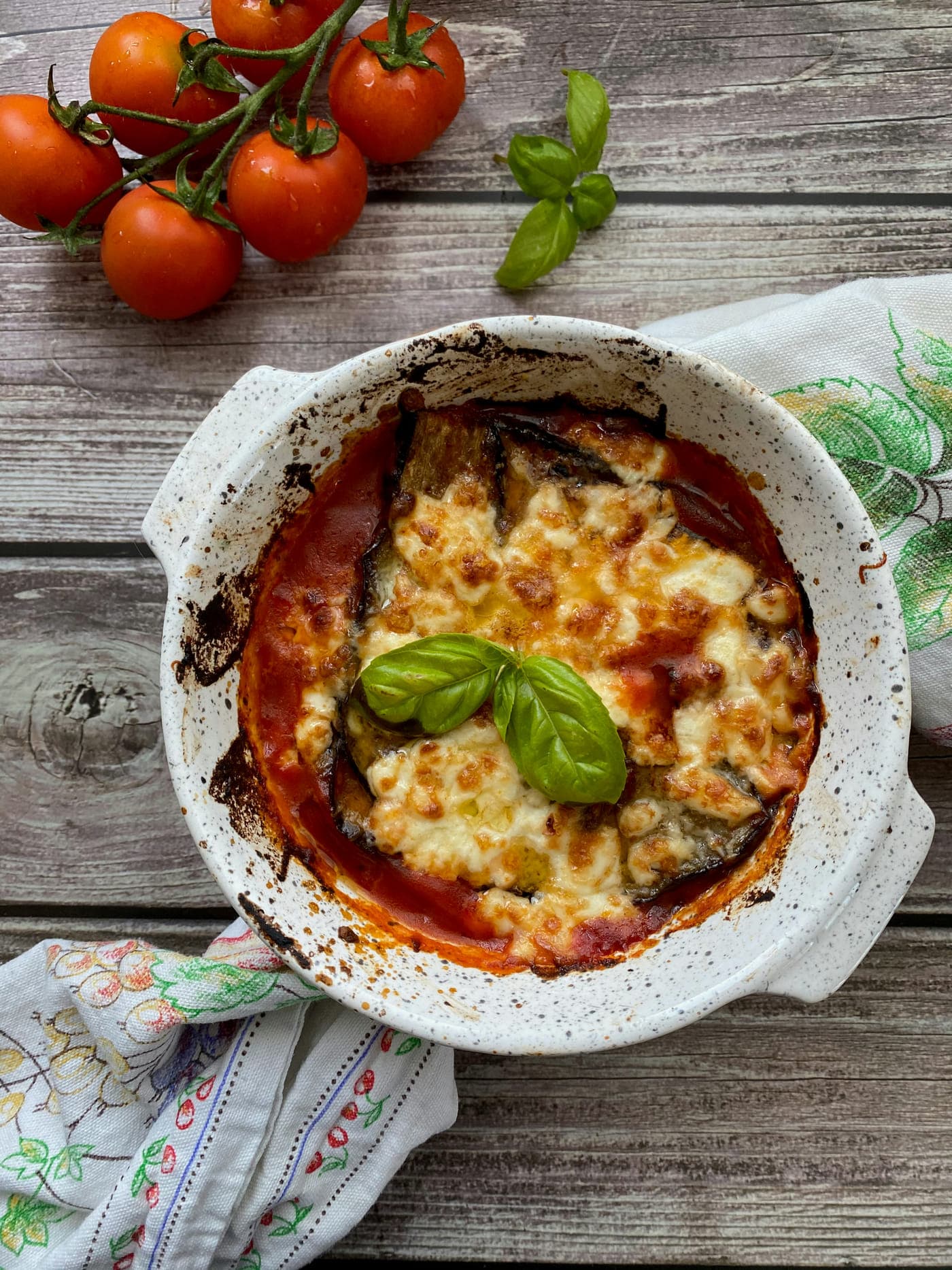 Baked aubergine parmigiana bubbling in a white dish, topped with basil